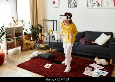 Una ragazza si diverte a casa indossando un top giallo e pantaloni bianchi, impegnata nel divertimento in realtà virtuale. Foto Stock