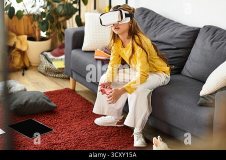 Una ragazza alfa-gen che indossa un visore VR si siede su un divano, immersa in un mondo digitale a casa. Foto Stock