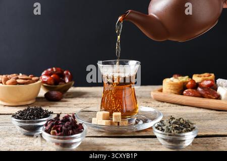 Versare il tè turco appena preparato nel bicchiere al tavolo di legno, primo piano Foto Stock