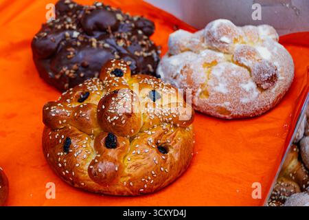 Primo piano dei tre pani messicani del giorno dei morti, mostrando le tradizionali varietà di zucchero, sesamo e cioccolato, su un festoso sfondo arancione. Foto Stock