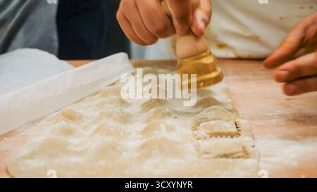 Sapienti mani che realizzano ravioli freschi con l'autentico strumento italiano per modellare l'impasto in un'affollata cucina del ristorante Foto Stock