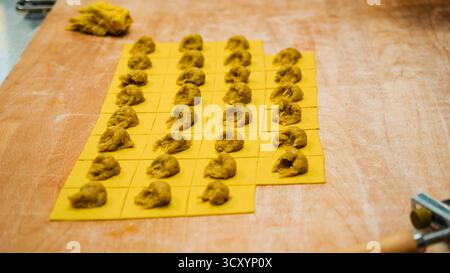 Una donna esperta che prepara sapientemente ripieno di ravioli freschi fatti in casa e pasta in un ambiente culinario vivace Foto Stock
