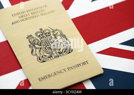 Passaporto d'emergenza britannico. Documento temporaneo di colore giallo su primo piano sullo sfondo della bandiera Foto Stock