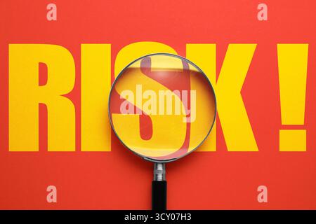 Rischio parola e lente di ingrandimento su sfondo rosso, vista dall'alto Foto Stock