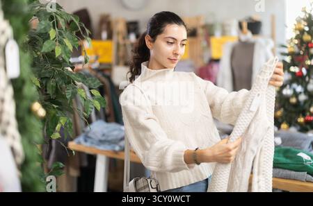 La donna armena si trova in un negozio decorato per Natale e prende un maglione caldo Foto Stock