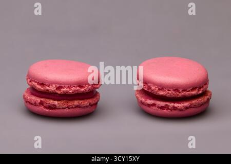 Due dessert al macaron rosa disposti insieme su sfondo grigio neutro. Composizione minimale per la pubblicità di prodotti da forno e design moderno del cibo. Foto Stock