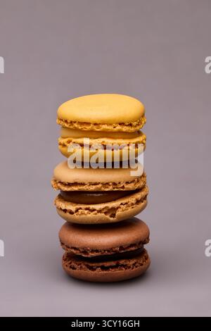 Pila verticale di quattro macaron colorati, tra cui cioccolato, arancio e giallo su superficie grigia. Composizione dessert minimalista per pasticceria b Foto Stock