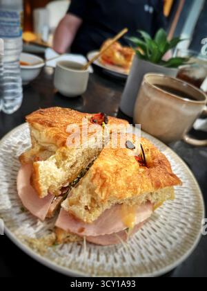 Delizioso sandwich con prosciutto e formaggio su un croissant servito con una tazza di caffè in un ambiente accogliente. Foto Stock