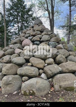 Una grande piramide di rocce impilate in una foresta che si radura con alberi e un cielo nuvoloso sullo sfondo Foto Stock