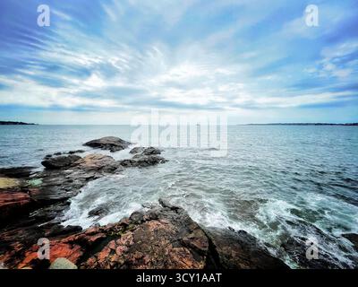 Costa rocciosa sotto un cielo nuvoloso con onde che si infrangono lungo la riva, creando un paesaggio marino sereno e suggestivo Foto Stock