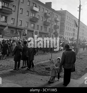 Una suggestiva foto d'archivio del 7 novembre 1974 cattura lo spirito di una parata dell'anniversario della rivoluzione d'ottobre a Sloviansk, RSS Ucraina. Una grande colonna di manifestanti, comprese famiglie con bambini, marcia lungo una strada acciottolata. I partecipanti portano bandiere sovietiche, ritratti di leader politici, striscioni con slogan come "Glory to the Heroes of Labor" e palloncini festivi. Questa immagine è un vivido documento di una grande festa di stato e della vita pubblica di un pacifico Donbas prima della guerra Foto Stock