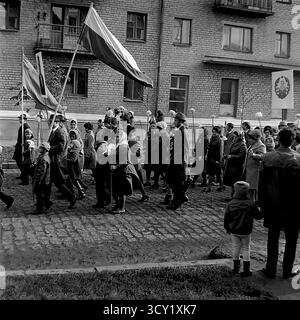 Una suggestiva foto d'archivio del 7 novembre 1974 cattura lo spirito di una parata dell'anniversario della rivoluzione d'ottobre a Sloviansk, RSS Ucraina. Una grande colonna di manifestanti, comprese famiglie con bambini, marcia lungo una strada acciottolata. I partecipanti portano bandiere sovietiche, ritratti di leader politici, striscioni con slogan come "Glory to the Heroes of Labor" e palloncini festivi. Questa immagine è un vivido documento di una grande festa di stato e della vita pubblica di un pacifico Donbas prima della guerra Foto Stock