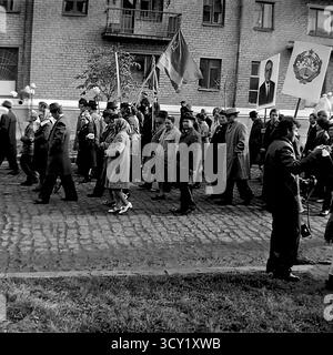Una suggestiva foto d'archivio del 7 novembre 1974 cattura lo spirito di una parata dell'anniversario della rivoluzione d'ottobre a Sloviansk, RSS Ucraina. Una grande colonna di manifestanti, comprese famiglie con bambini, marcia lungo una strada acciottolata. I partecipanti portano bandiere sovietiche, ritratti di leader politici, striscioni con slogan come "Glory to the Heroes of Labor" e palloncini festivi. Questa immagine è un vivido documento di una grande festa di stato e della vita pubblica di un pacifico Donbas prima della guerra Foto Stock