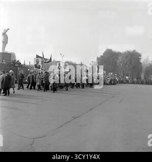 Una suggestiva foto d'archivio del 7 novembre 1974 cattura una dimostrazione su larga scala per l'anniversario della Rivoluzione d'ottobre a Sloviansk. Colonne di cittadini, comprese famiglie e una banda di ottoni, marciano attraverso le strade e la piazza centrali della città. Portano con orgoglio bandiere sovietiche, striscioni e grandi ritratti di Lenin e di altri leader politici. Questa immagine è un vivido documento di una grande festa di stato, che mostra lo spirito collettivo e la vita pubblica di un pacifico Donba prima della guerra Foto Stock