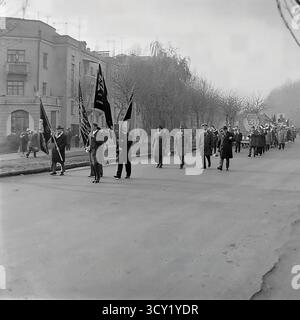 Una suggestiva foto d'archivio del 7 novembre 1974 cattura una dimostrazione su larga scala per l'anniversario della Rivoluzione d'ottobre a Sloviansk. Colonne di cittadini, comprese famiglie e una banda di ottoni, marciano attraverso le strade e la piazza centrali della città. Portano con orgoglio bandiere sovietiche, striscioni e grandi ritratti di Lenin e di altri leader politici. Questa immagine è un vivido documento di una grande festa di stato, che mostra lo spirito collettivo e la vita pubblica di un pacifico Donba prima della guerra Foto Stock
