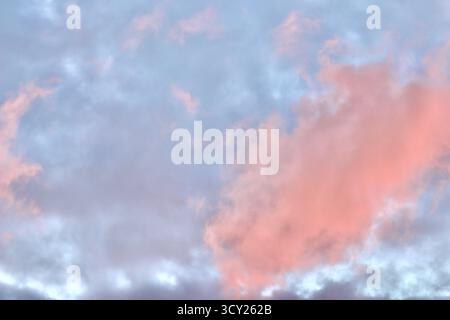 Un'atmosfera da sogno in cui una massa drammatica di nuvole di rosa e pesca si illumina contro una malva pallida e il cielo blu durante il tramonto o l'alba, riempiendosi Foto Stock