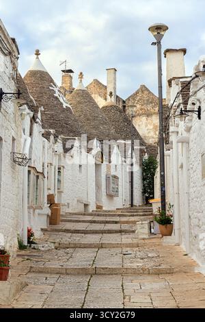 Una tranquilla vista mattutina delle strade vuote di Alberobello, Puglia, Italia. Le tradizionali case dei Trulli bianchi con i loro tetti conici fiancheggiano il Foto Stock