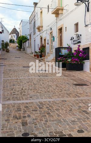 Una tranquilla vista mattutina delle strade vuote di Alberobello, Puglia, Italia. Le tradizionali case dei Trulli bianchi con i loro tetti conici fiancheggiano il Foto Stock