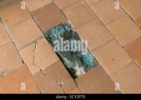 Una vista ravvicinata rivela le piastrelle rotte e incrinate di un pavimento trascurato. Le piastrelle sono in cattive condizioni, alcune mostrano macchie blu e mi Foto Stock