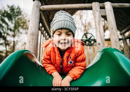 Ragazzo felice che gioca su uno scivolo in inverno Foto Stock