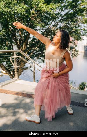 Donna ballerina in posa con le braccia allungate in un ambiente urbano Foto Stock