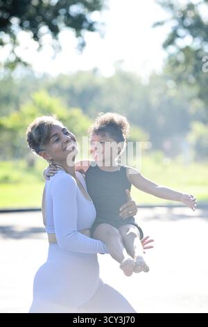 Donna sorridente che tiene un bambino felice all'aperto sotto la luce del sole. Foto Stock