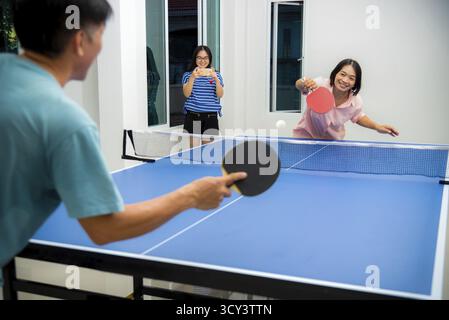 Divertimento di coppia giocando a ping pong o Ping pong al coperto insieme tempo libero con la competizione in giochi sportivi in casa. Padre madre e figlia famiglia asiatica Foto Stock