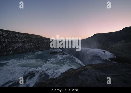 Vista della potente cascata Gullfoss che sfreccia giù per una gola rocciosa sotto un sereno cielo crepuscolo, Reykjavík, Islanda. Foto Stock