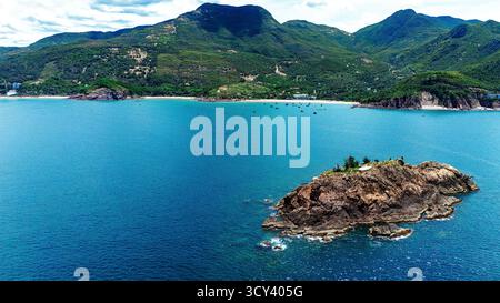 Panorama aereo dell'isolotto roccioso circondato dal Mar Blu con costa montuosa sullo sfondo, Quy Nhon, Vietnam Foto Stock