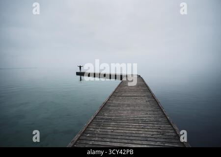 Uomo con le braccia alzate contro la luce alla fine di un molo sul mare alla luce della sera Foto Stock