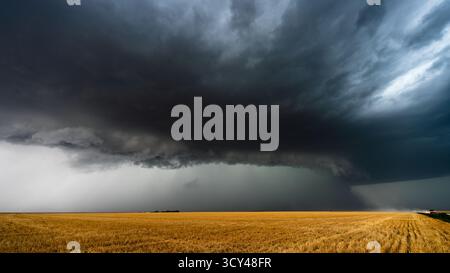 Una grande e potente tempesta incombe sui campi mentre le auto percorrono una strada polverosa, con un cielo spettacolare, nuvole in movimento, ombre e atmosfere mostruose che catturano una bellezza epica Foto Stock