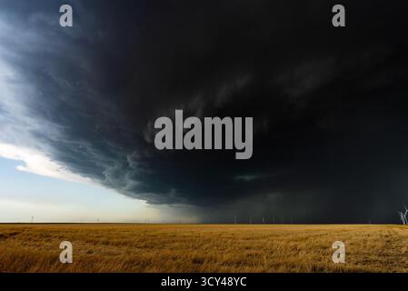 Nuvole di tempesta rotolano nel cielo sopra campi dai colori caldi e un parco eolico, creando una scena drammatica e lunare piena di texture, movimento, atmosfera, Foto Stock