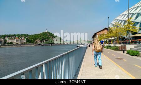 Budapest, Ungheria - 23 aprile 2018 - giovane escursionista che cammina lungo il danubio a budapest con ponte sullo sfondo. Foto Stock
