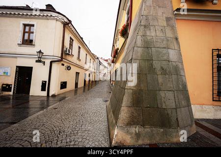 Tarnow, Polonia - 10 ottobre 2025: Ampia vista su una stretta strada acciottolata di Tarnow, con edifici pastello e un alto monumento in pietra. Foto Stock