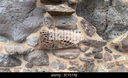 Primo piano della parete in stucco invecchiato che mostra pietre vulcaniche ruvide e dettagli della superficie incrinata Foto Stock