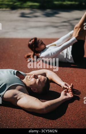 Coppie diverse di atleti che si rilassano sulla pista all'aperto dopo una vigorosa sessione di allenamento Foto Stock