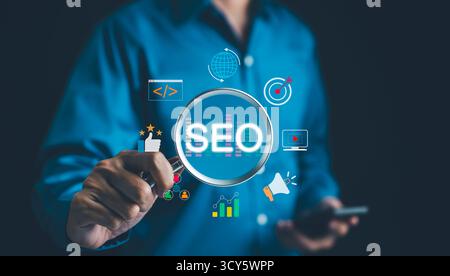 SEO Search Engine Optimization (Ottimizzazione motore di ricerca SEO). L'uomo d'affari tiene una lente d'ingrandimento che mette in risalto il SEO, circondato da varie icone del marketing digitale, Foto Stock