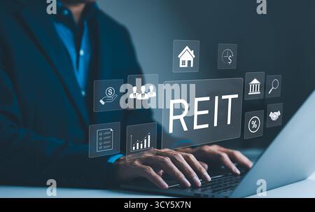 REIT, concetto di fiducia per gli investimenti immobiliari. Un uomo d'affari lavora su un laptop con icone che rappresentano il Real Estate Investment Trust, Foto Stock