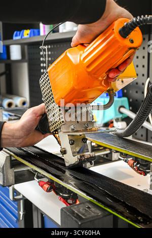 Assistenza professionale a mano su una base per sci con applicatore di cera calda in officina. Foto Stock