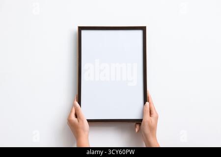 Donna che appende una cornice vuota per diplomi su un muro bianco, primo piano. Mockup per il design Foto Stock