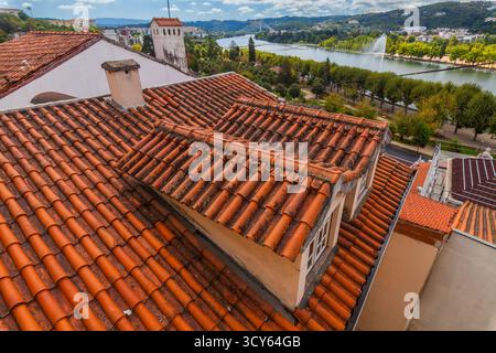 Una vista ad alto angolo cattura i tetti di terracotta intemprati che si affacciano su un fiume panoramico, lussureggianti parchi verdi e un paesaggio urbano lontano sotto una parzialmente nuvolosa Foto Stock