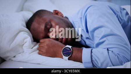 Uomo con smartwatch che rintraccia il sonno nel letto confortevole Late Night. Professioni possibili: Atleta, Personal Trainer, Dottore Foto Stock