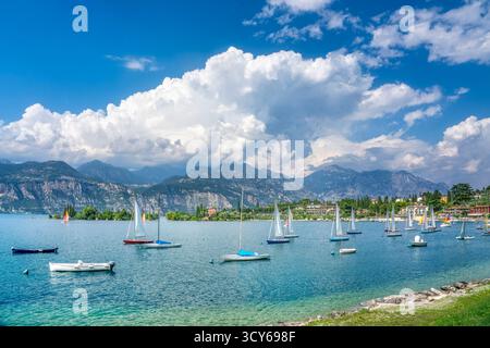 Barche a vela ancorate nelle acque turchesi della baia della Val di sogno a Malcesine, Lago di Garda. Montagne spettacolari e nuvole bianche sul lago alpino italiano, Ven Foto Stock