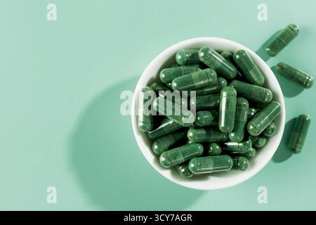 Capsule di spirulina verde in ciotola bianca su menta background.Organic supplemento superfood per disintossicazione, energia, supporto immunitario Foto Stock