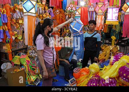 Mumbai, India. 17 ottobre 2025. Una donna (L) che indossa una maschera protettiva controlla una lanterna davanti a Diwali, la festa indù delle luci per le strade di Mumbai. Diwali è il festival delle luci celebrato dagli indù in tutto il paese. La gente pulisce la propria casa, disegna un rangoli (una forma d'arte tradizionale indiana dove vengono realizzati vari disegni sul pavimento), acquista lanterne, nuovi vestiti, dolci e spuntini. Illuminano le loro case con lampade di terra che segnano la vittoria della luce sull'oscurità. (Foto di Ashish Vaishnav/SOPA Images/Sipa USA) credito: SIPA USA/Alamy Live News Foto Stock