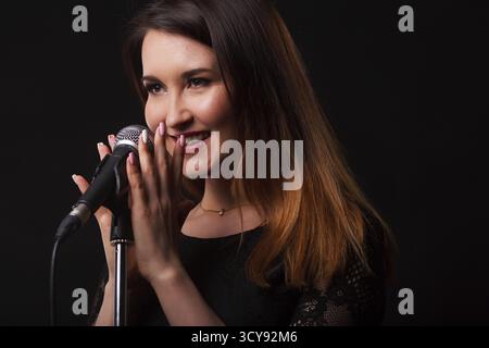 Bella donna con microfono in mani su sfondo di fumo in studio Foto Stock