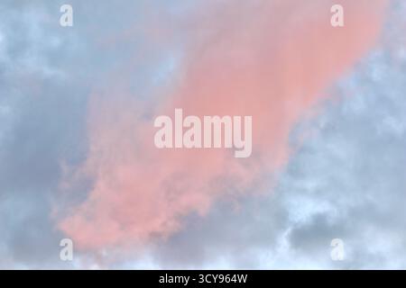 Un'atmosfera da sogno in cui una massa drammatica di nuvole di rosa e pesca si illumina contro una malva pallida e il cielo blu durante il tramonto o l'alba, riempiendosi Foto Stock