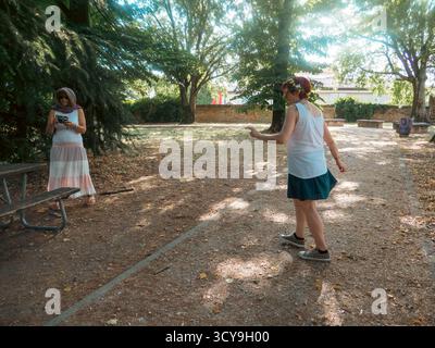 Due donne che si godono una giornata di sole all'aperto interagendo giocosamente in un parco con alberi e luce solare attenuata creando un'atmosfera rilassata per la vita Foto Stock