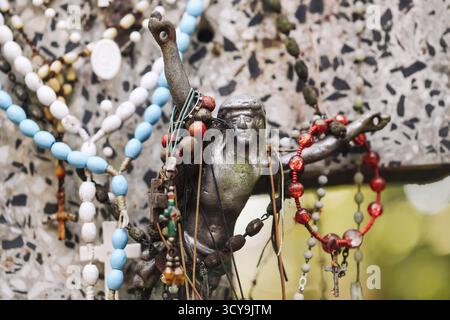 Tomba abbandonata con statua di Gesù intemprata ricoperta di rosari e perline di preghiera. Cimitero religioso simbolo che mostra fede memoria devozione e decadenza. Foto Stock