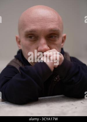 Ritratto ravvicinato di un uomo pensivo con nanismo, mani strette, copertura mento e sguardo lontano, appoggiato su un parapetto. Persona unica con un'attenzione particolare, s Foto Stock
